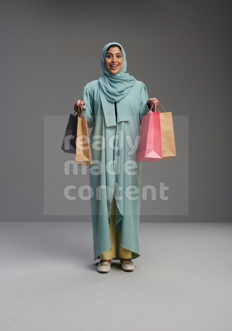 Saudi Woman wearing Abaya standing holding shopping bag on Gray background