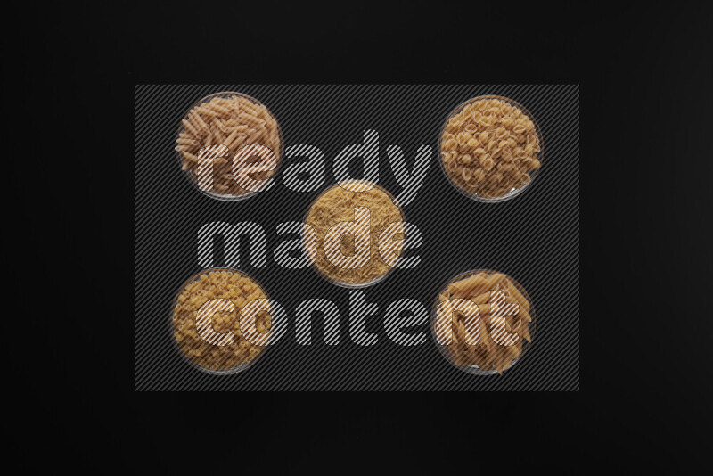 Different pasta types in 5 glass bowls on black background