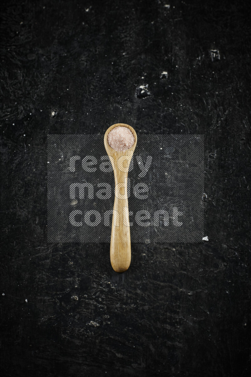 A wooden spoon full of pink himalayan salt on black background
