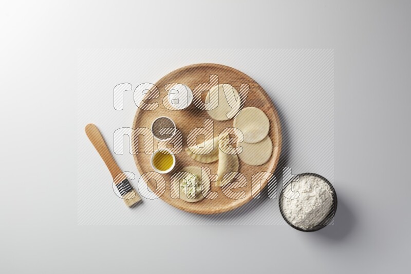 two closed sambosas and one open sambosa filled with cheese while flour, salt, black pepper and oil with oil brush aside in a wooden dish on a white background