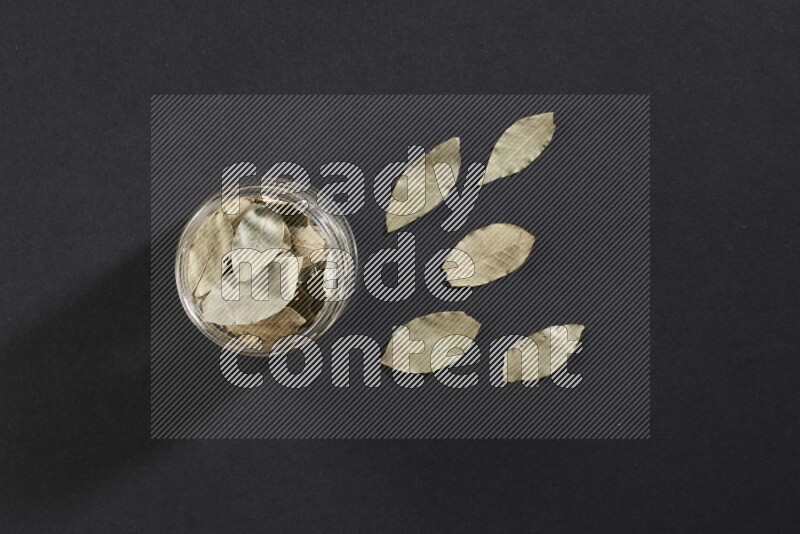 A glass jar filled with dried bay leaves on black flooring