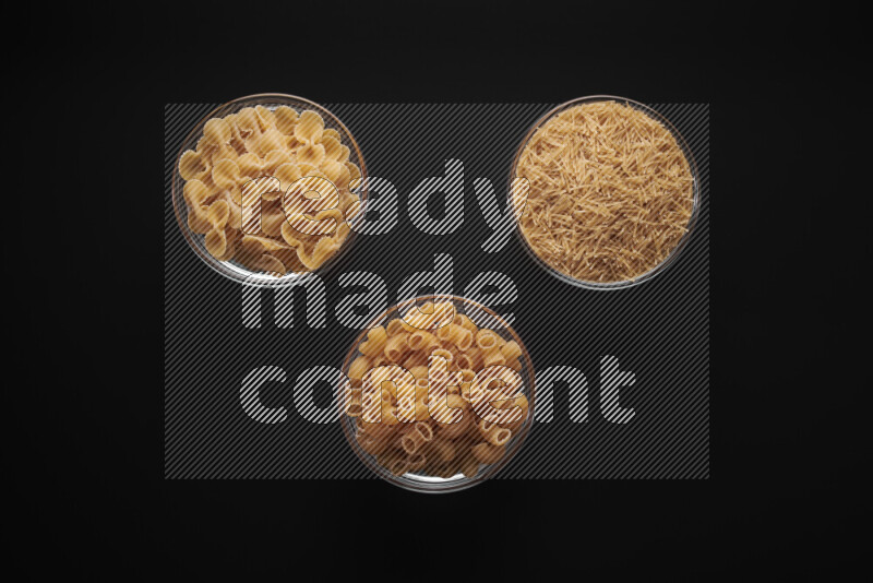 Different pasta types in glass bowls on black background