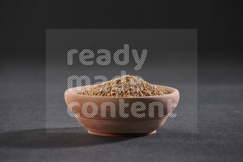 A wooden bowl full of mustard seeds on a black flooring