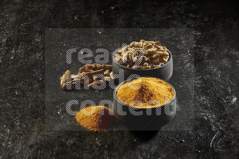 وعاءان من الفخار باللون الأسود، أحدهما ممتلئ ببودرة الكركم والآخر ممتلئ بأصابع كاملة من الكركم المجفف على خلفية سوداء