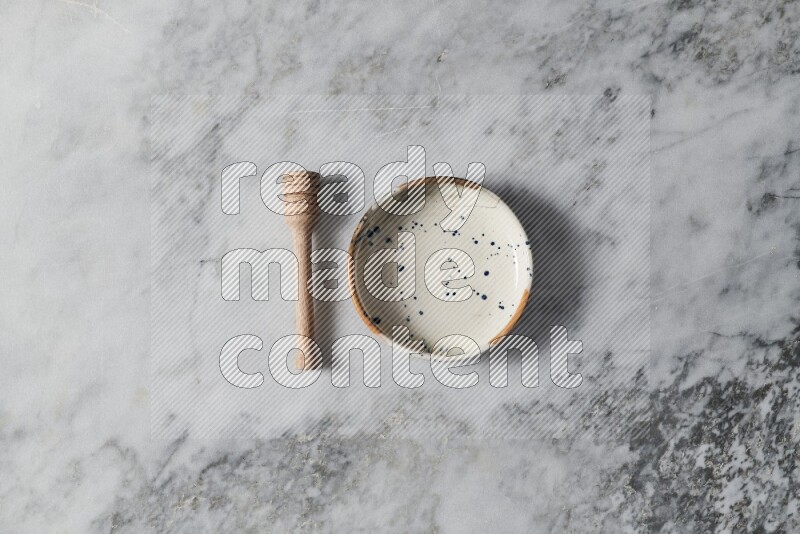 Multicolored pottery bowl with wooden honey dipper on the side on grey marble background