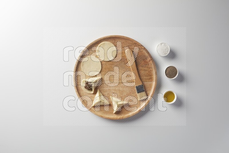 two closed sambosas and one open sambosa filled with meat while salt, black pepper and oil with oil brush aside in a wooden dish on a white background