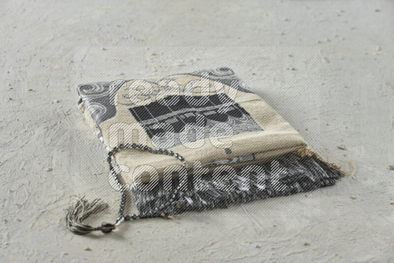 A folded prayer mat with different elements such as quran and prayer beads on white textured background