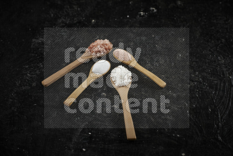 4 wooden spoons filled with fine and coarse salt on black background