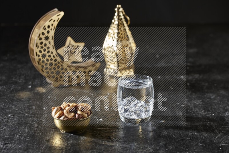Nuts in a metal bowl with water beside golden lanterns in a dark setup