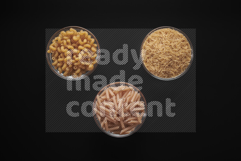Different pasta types in glass bowls on black background