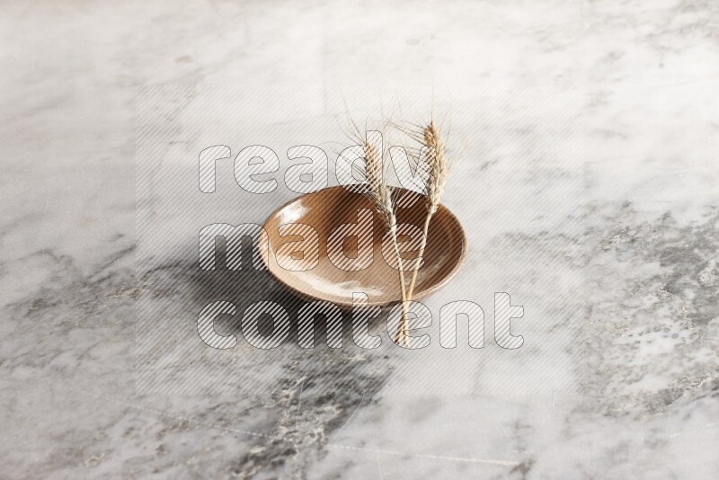 Wheat stalks on multicolored pottery plate on grey marble background