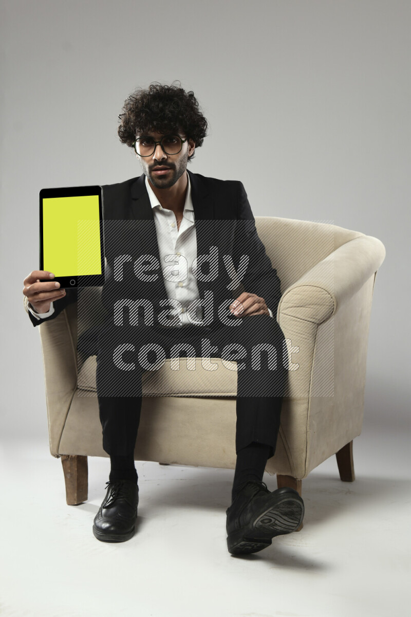 A man wearing formal sitting on a chair showing a tablet screen on white background