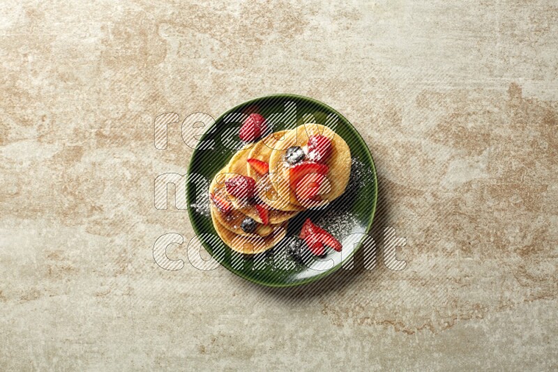 Five stacked mixed berries mini pancakes in a green plate on beige background