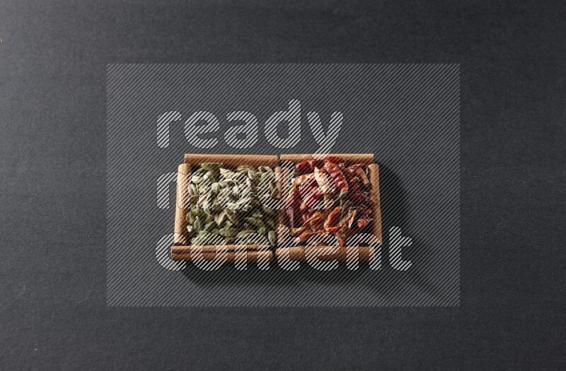 مربعان من أعواد القرفة ممتلئان بالفلفل الحار المجفف وحبوب الهيل علي خلفية سوداء