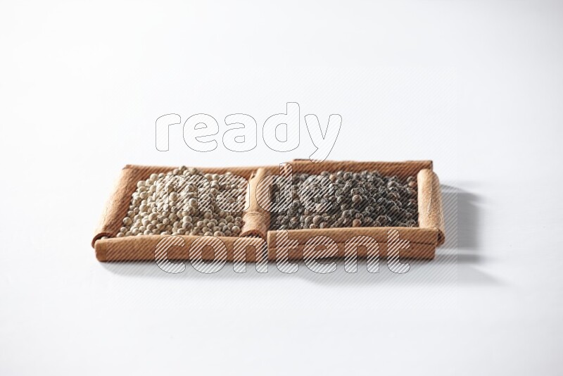 2 squares of cinnamon sticks full of black pepper and white pepper on white flooring