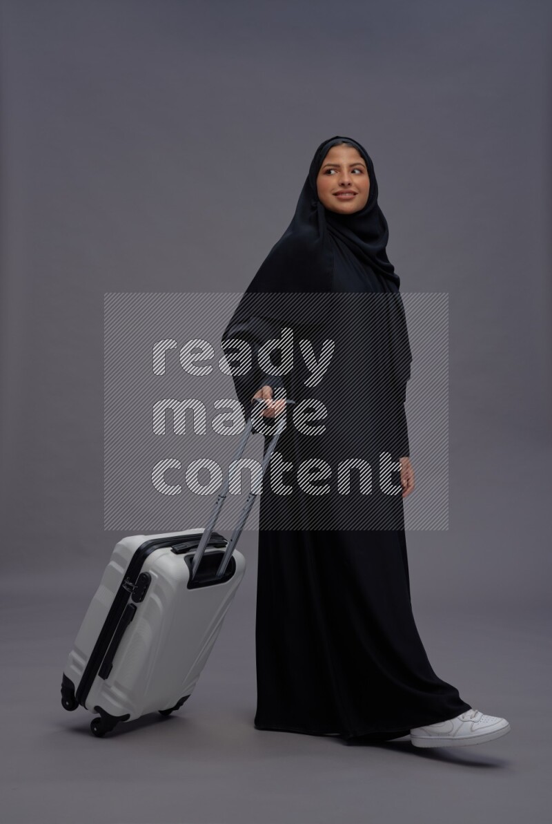Saudi woman wearing Abaya standing holding bag on gray background