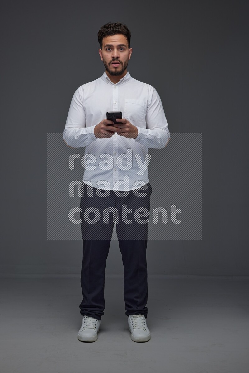 A man wearing smart casual standing and using his phone eye level on a gray background