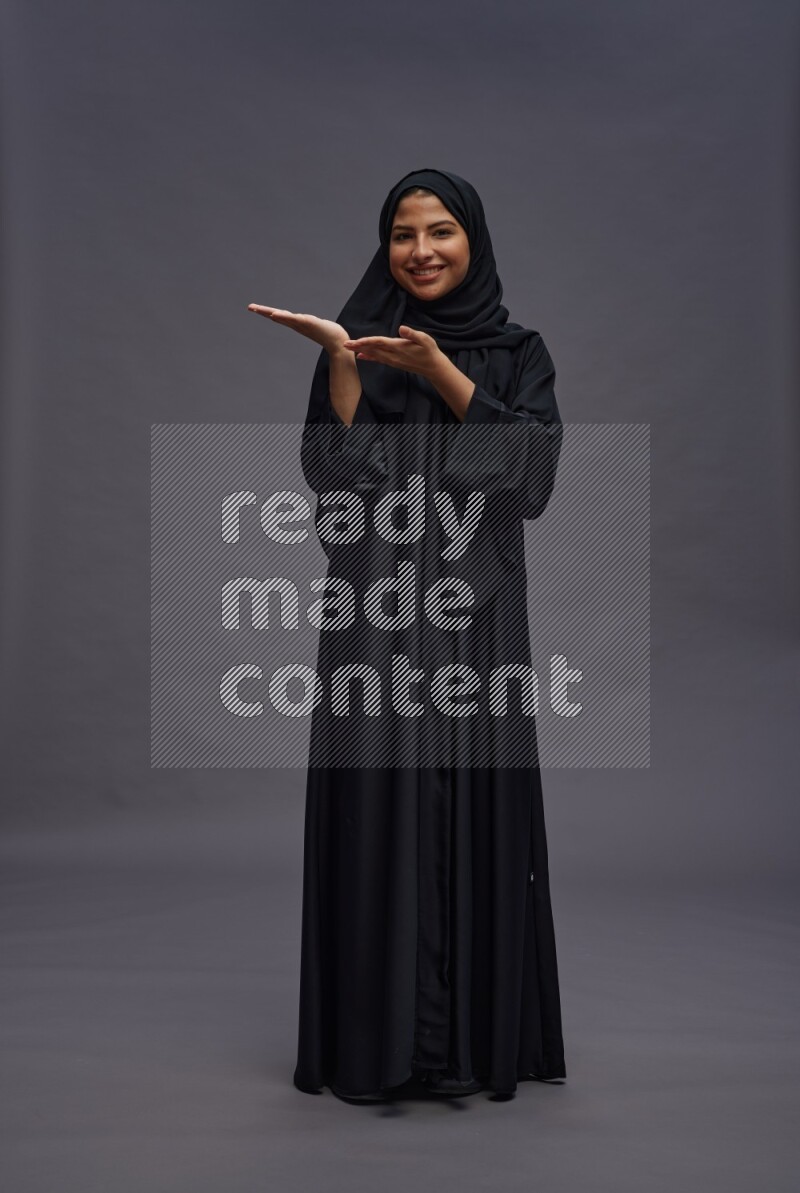 Saudi woman wearing Abaya standing interacting with the camera on gray background