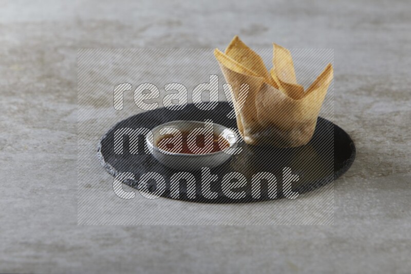 wonton cups with soy sauce ramkin on circle slate on grey textured counter top