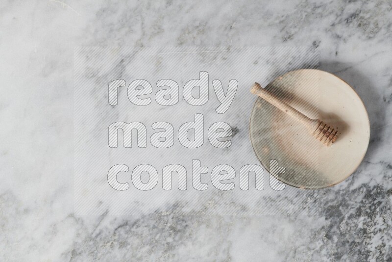 Multicolored pottery plate with wooden honey dipper in it on grey marble background