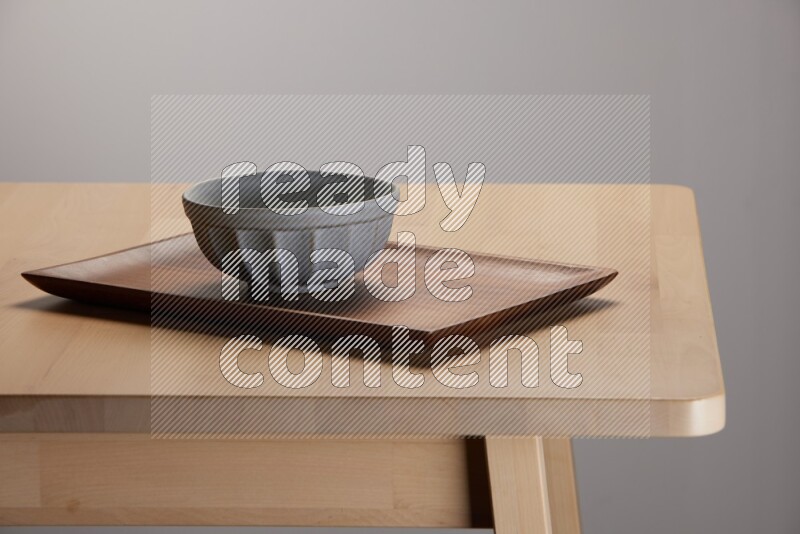 grey bowl placed on a rectangular wooden tray on the edge of wooden table
