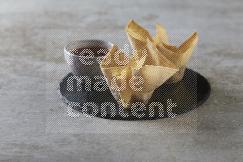 wonton cups with soy sauce ramkin on circle slate on grey textured counter top