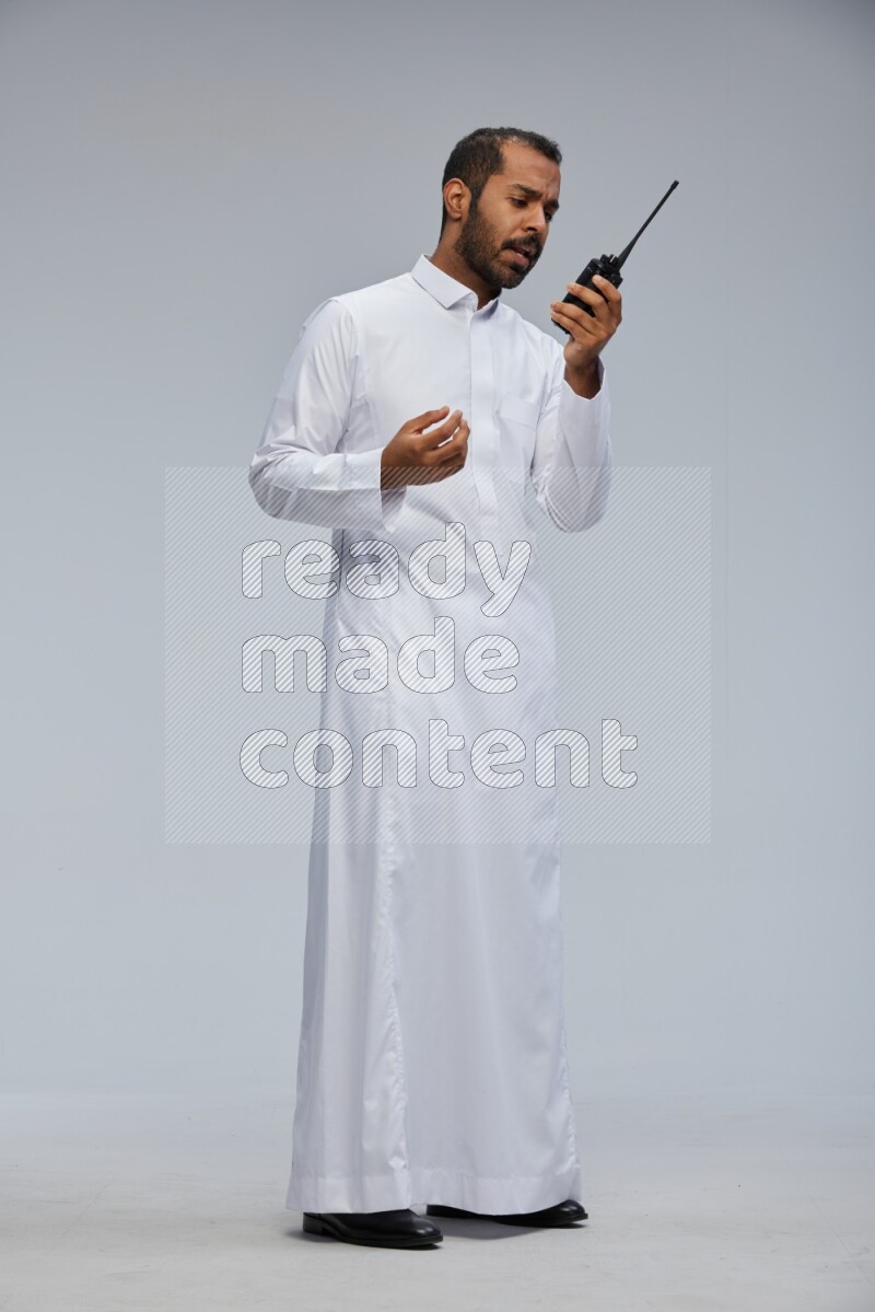 Saudi man Wearing thob standing holding walkie-talkie on Gray background