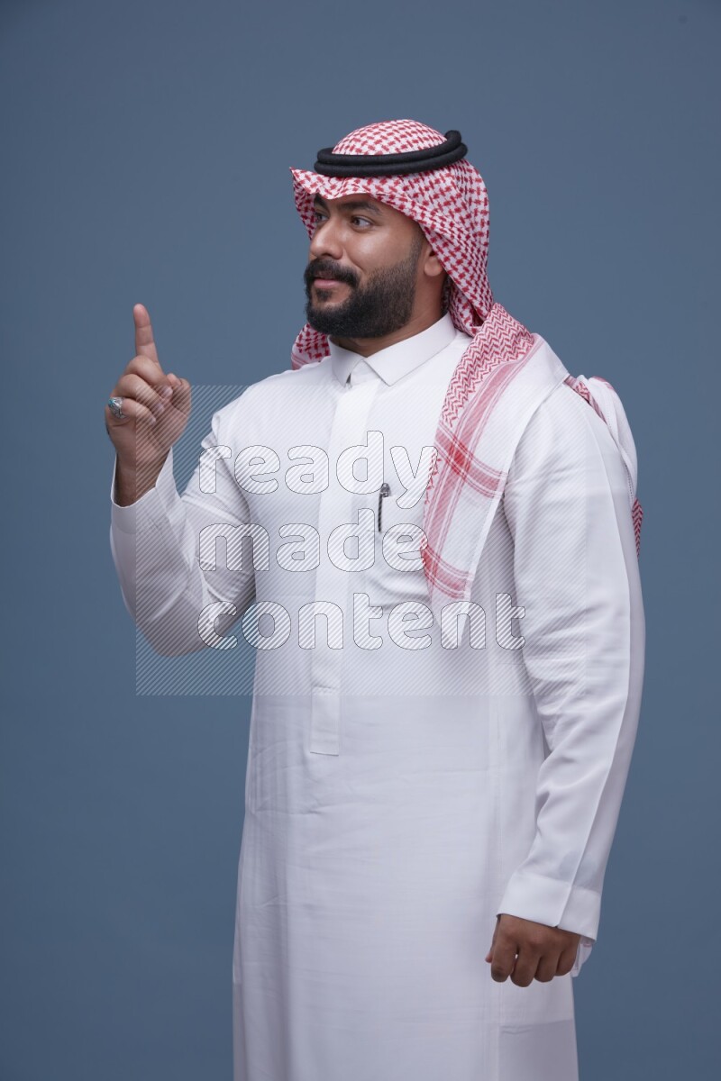 A Saudi man posing on blue background wearing Thob and Shomag