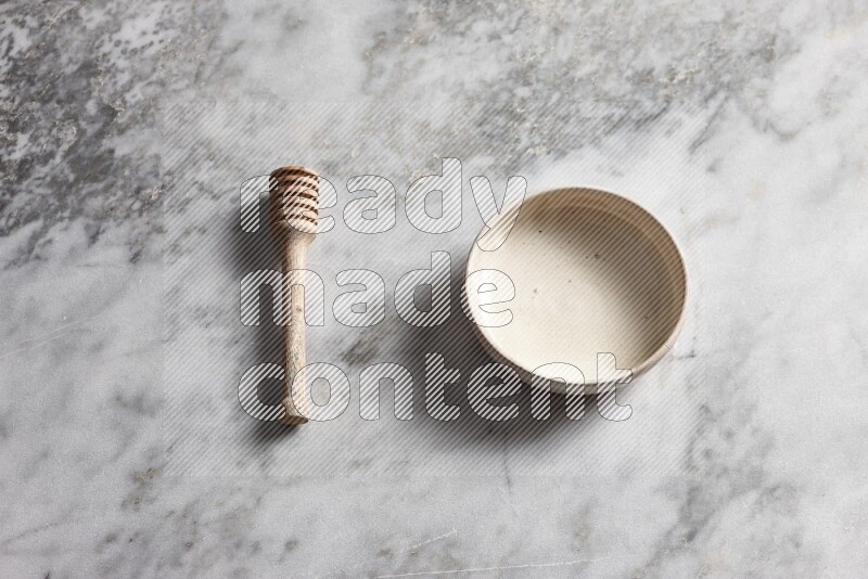 Beige pottery bowl with wooden honey dipper on the side on grey marble background