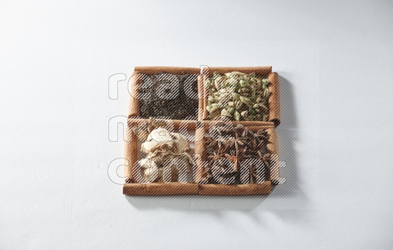 4 squares of cinnamon sticks full of tea, cardamom, star anise and ginger on white flooring