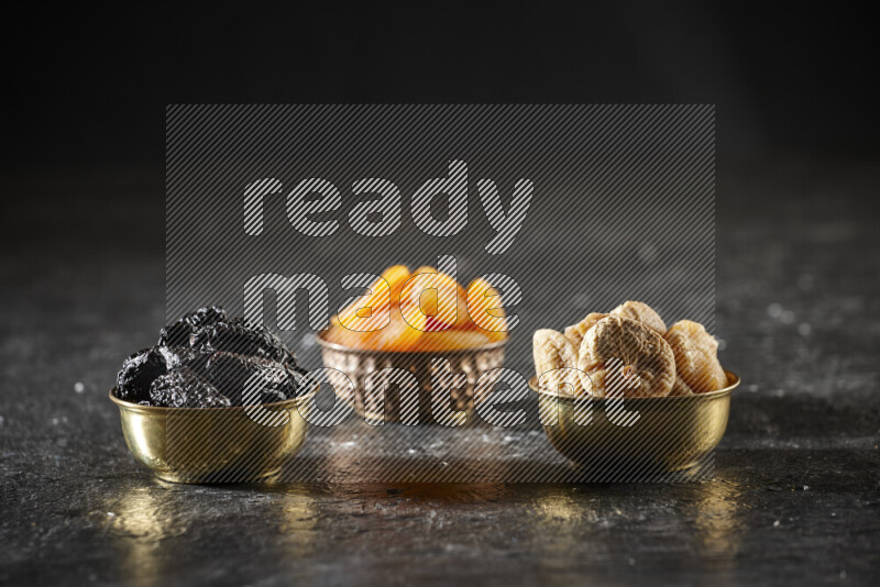 Dried fruits in metal bowls in a dark setup