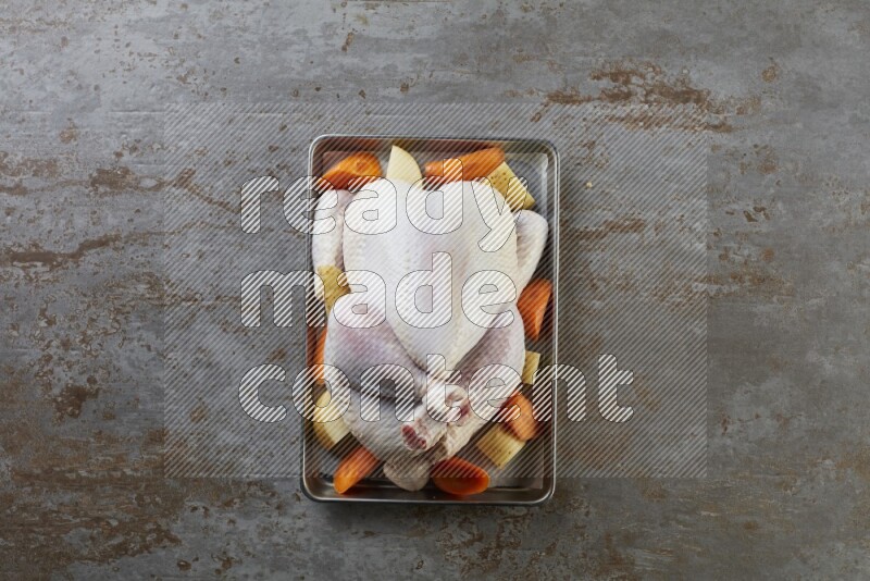 whole Raw chicken on a small oven trey direct on a rustic grey background