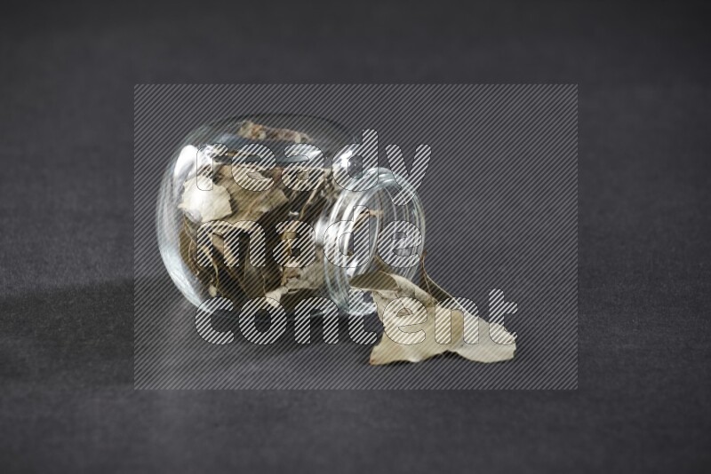 وعاء زجاجي ممتلئ بأوراق الغار والوعاء مقلوب وبعض الأوراق متناثرة خارجه علي خلفية سوداء