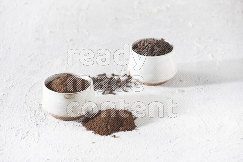 2 Beige ceramic bowls, one full of cloves and the other full of powder on textured white flooring