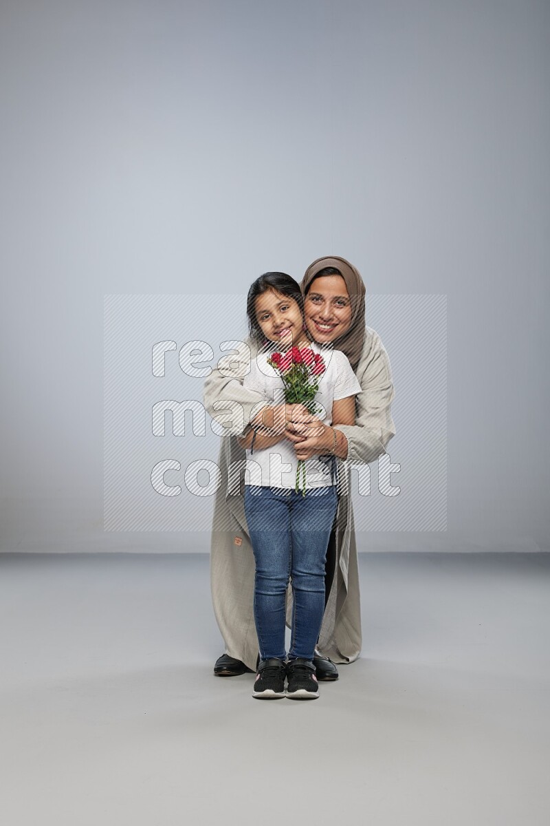 A girl standing giving flowers to her mother on gray background
