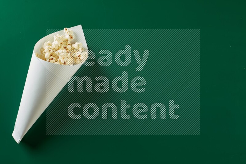 A paper cone full of popcorn on a green background in a top veiw shot