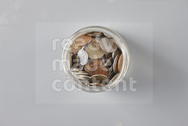 Random old coins in a glass jar on grey background