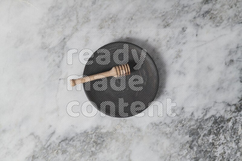 Black pottery plate with wooden honey dipper in it on grey marble background