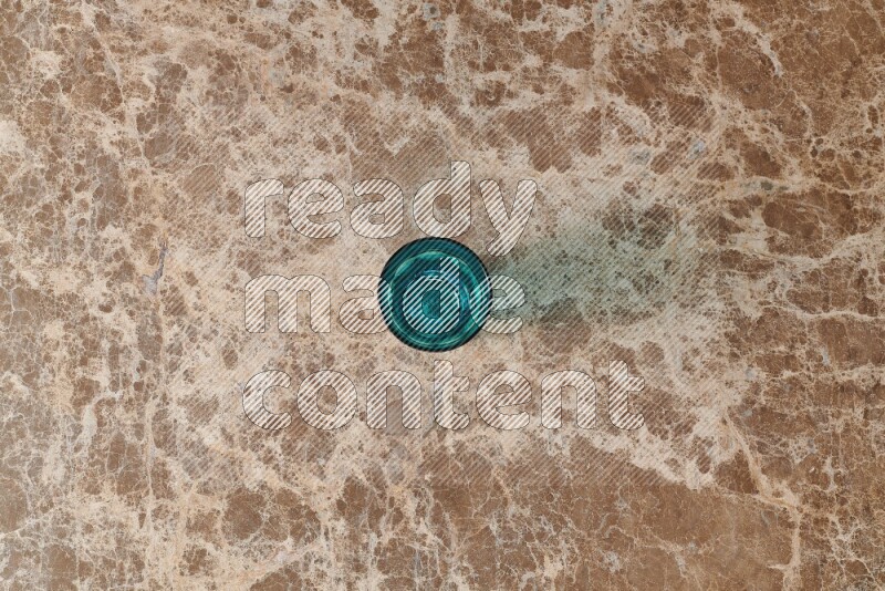 A turquoise glass cup on beige marble background