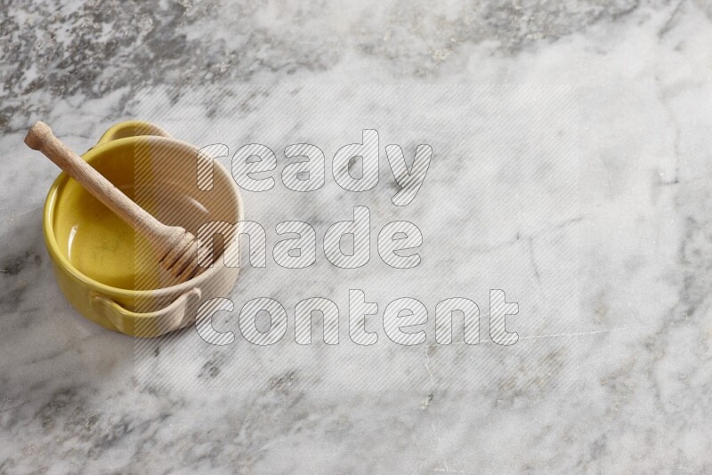 Multicolored pottery bowl with wooden honey dipper in it on grey marble background