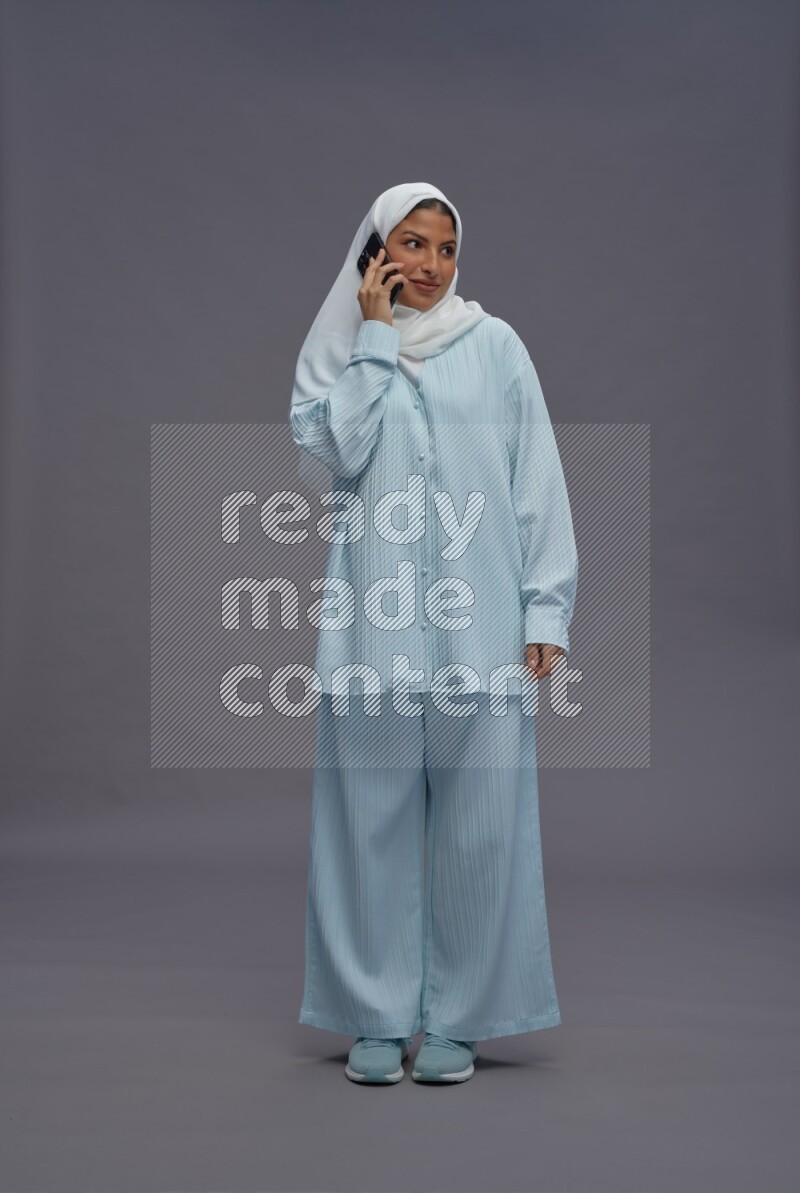 Saudi woman wearing hijab clothes standing talking on phone on gray background