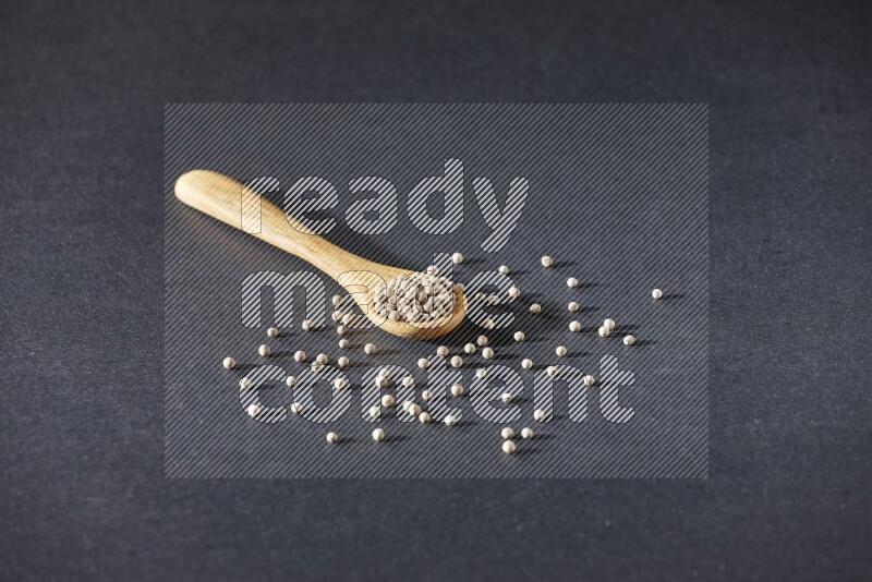 A wooden spoon full of white pepper beads on black flooring