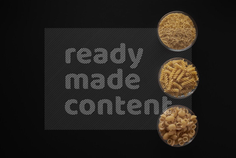 Different pasta types in 3 glass bowls on black background