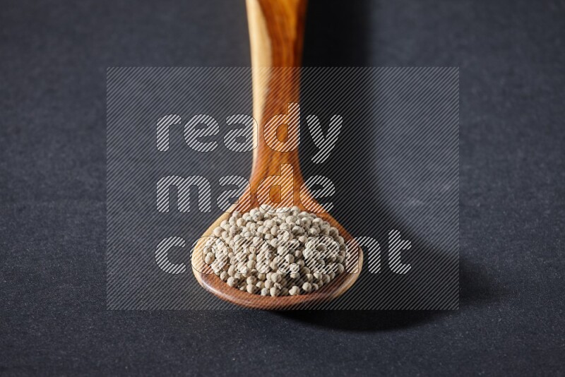 A wooden ladle full of white pepper beads on black flooring