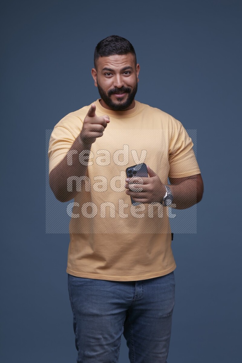 A man Pointing at a Smartphone on Blue Background wearing Orange T-shirt