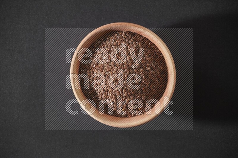A wooden bowl full of flaxseeds on a black flooring