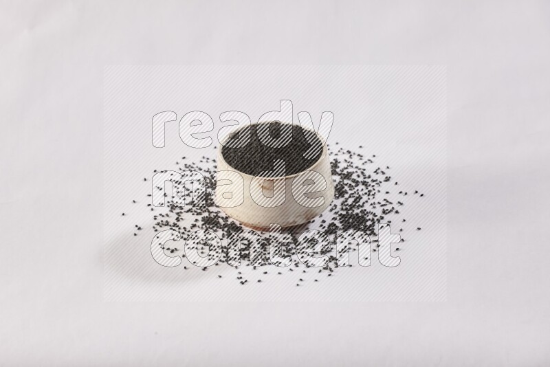 A beige pottery bowl full of black seeds and more seeds spread on a white flooring