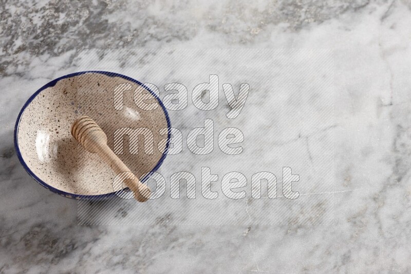 Multicolored pottery bowl with wooden honey dipper in it on grey marble background