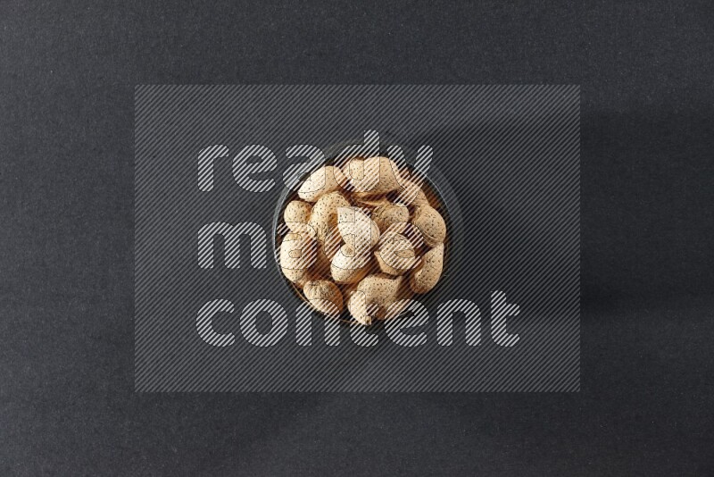 A black pottery bowl full of almonds on a black background in different angles
