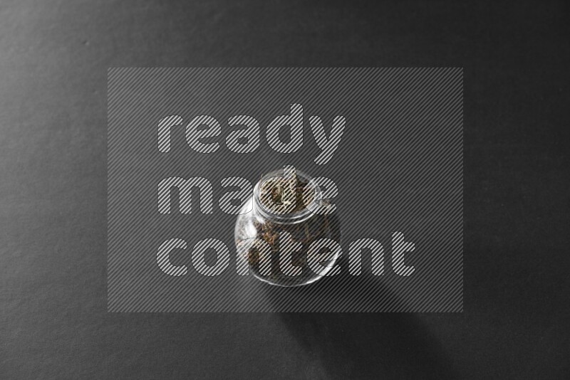 A glass spice jar full of basil on black flooring